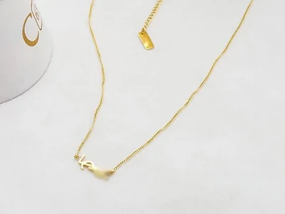 Collar fino dorado con un pequeño colgante, junto a un cono blanco de exposición