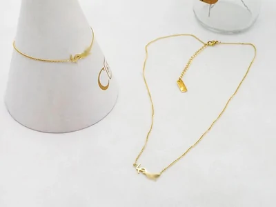 Collar fino dorado con un pequeño colgante, junto a un cono blanco de exposición